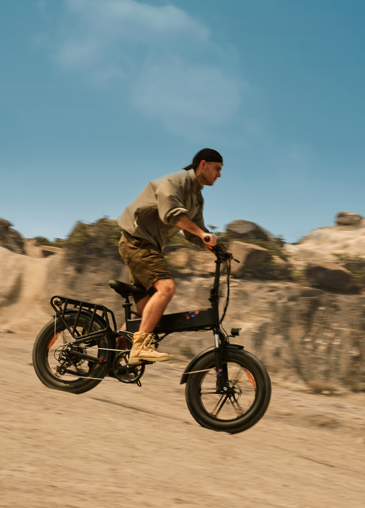 a man rides a black engwe engine pro folding e-bike on the sand